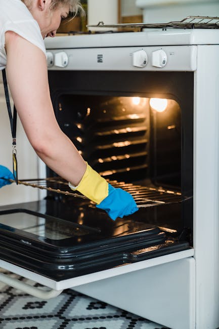 Close-up of a modern kitchen with a stainless steel oven built into white cabinetry, partially open oven door revealing a clean interior, situated beneath a grey countertop. The countertop extends alo